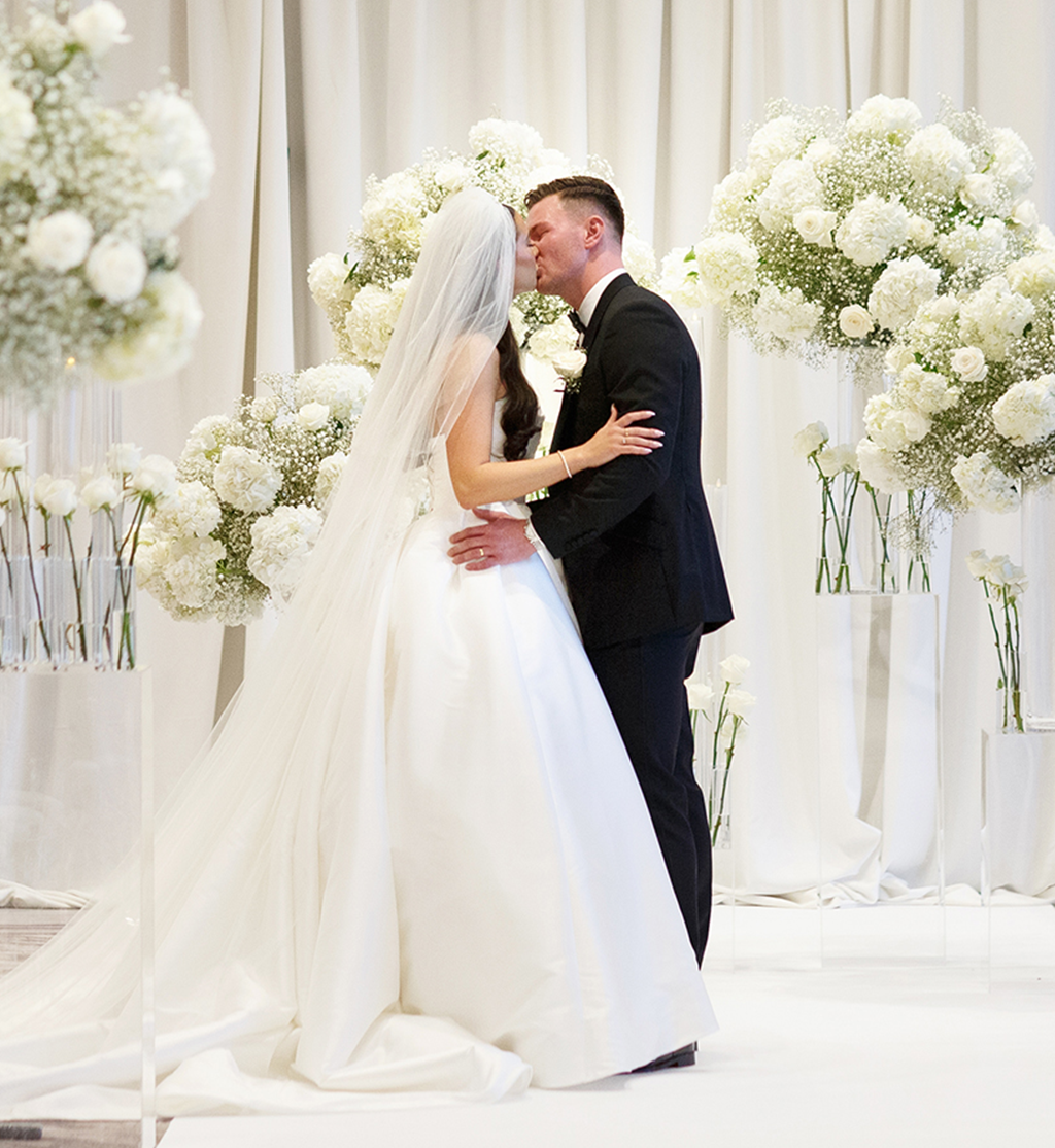 Bride and groom kissing on white aisle with floral plinths at Cameron House by Muse Styling