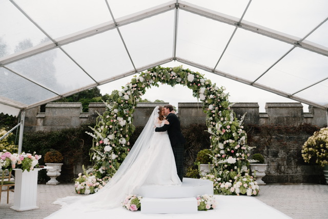 Newly married couple sharing their first kiss surrounded by bespoke floral installations at Dundas Castle